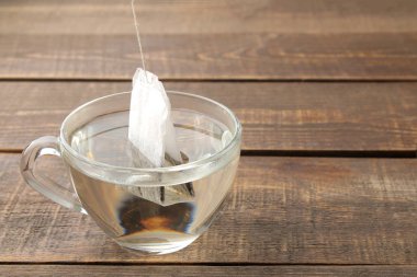 Kahverengi ahşap arka plan üzerinde bir cam fincan çay poşeti. çay yapmak için