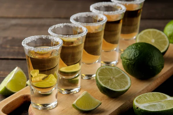 gold tequila in a glass shot glass with salt and lime on a brown wooden background. bar. alcoholic beverages