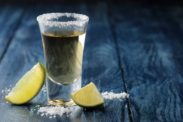 gold tequila in glass glass with salt and lime close up on blue wooden background. bar. alcoholic beverages. place for text