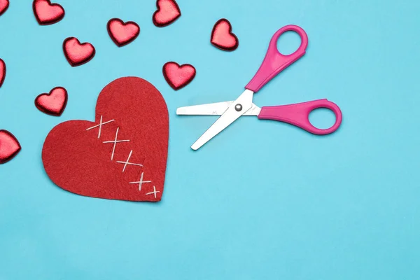 Broken red heart and small hearts with scissors on a bright blue background. view from above