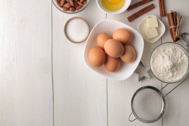 baking ingredients. baking tools. butter, eggs, sugar, milk, cinnamon, almonds on a white wooden background. view from above