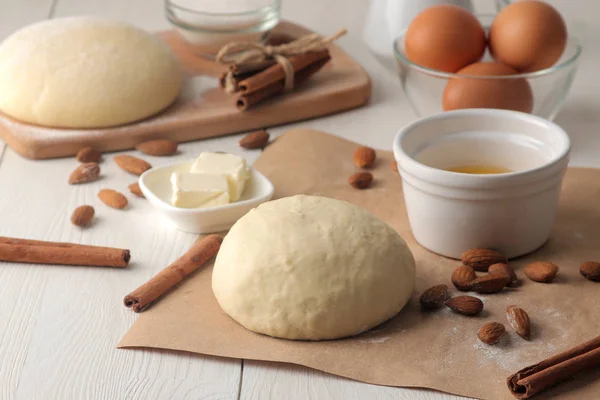 baking ingredients. baking tools. dough and butter, eggs, sugar, milk, cinnamon, almonds on a white wooden background