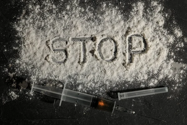 addictive drugs. heroin in a syringe and the inscription stop cocaine on a black table. The concept of drug addiction. view from above
