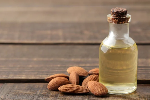 natural almond oil in a glass bottle and fresh almond nuts close-up on a brown wooden table. space for text