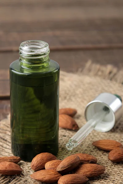 natural almond cosmetic oil in a glass bottle and fresh almond nuts close-up on a brown wooden table.