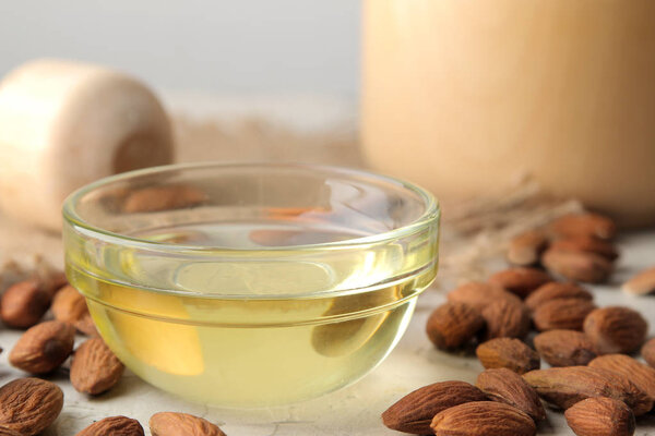 natural almond oil in a glass jar and fresh almond nuts on a light concrete background. close-up
