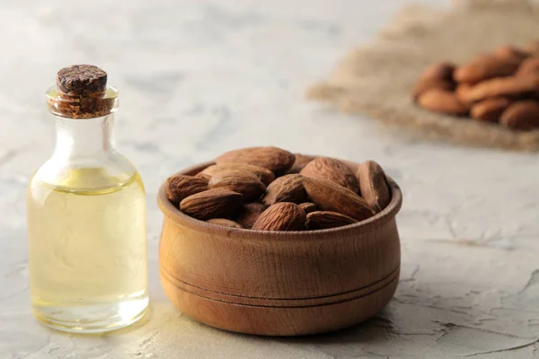 natural almond oil in a glass jar and fresh almond nuts on a light concrete background. close-up