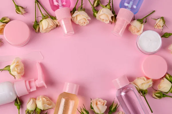 cosmetics for face and body in pink bottles with fresh roses on a delicate pink background. view from above. space for text
