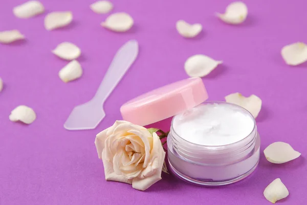face and body care cosmetics in pink bottles with fresh roses on a bright trendy purple background. cream in rosebuds. spa.