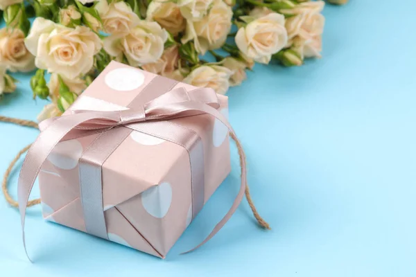 Beautiful mini roses with a pink gift box on a bright blue background. holidays. Valentine\'s Day. close-up