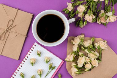 Bir not defteri ve bir fincan kahve parlak Lila arka plan üzerinde bir zarf içinde güzel mini gül. tatil. Sevgililer günü. Kadınlar günü. yukarıdan görüntülemek.