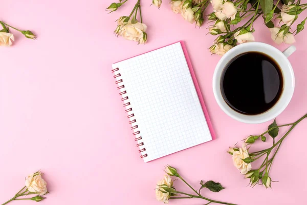 Beautiful mini roses with a cup of coffee and a notebook on a bright pink background. holidays. Valentine\'s Day. women\'s Day. view from above. space for text