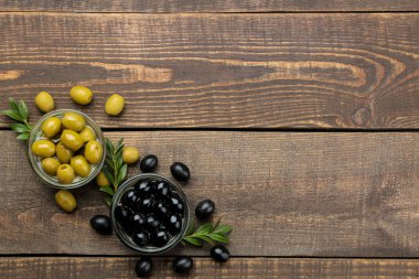 Yeşil ve siyah zeytin kahverengi ahşap bir masa üzerinde bir cam kabın içinde yapraklarla. yukarıdan görüntüleyin. metin için yer