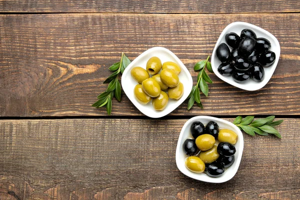 Yeşil ve siyah zeytin kahverengi ahşap bir masa üzerinde beyaz bir kase içinde yapraklarla. üstten görünüm. metin için yer