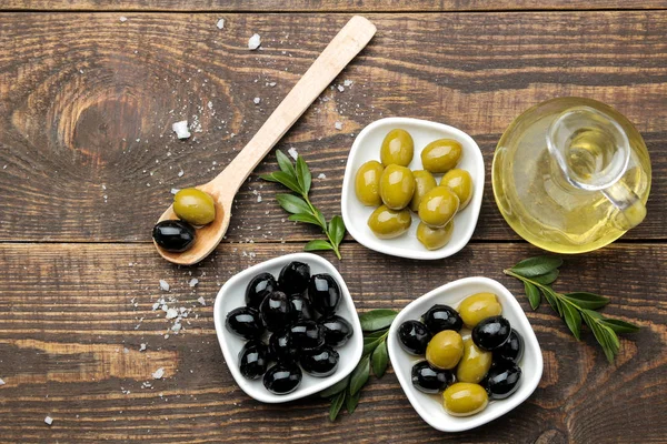 Green and black olives with leaves in a white bowl with olive oil on a brown wooden table. top view.