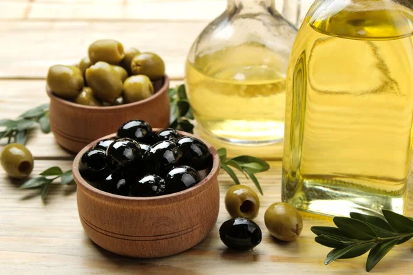 green and black olives in a wooden bowl with olive oil on a natural wooden table. close-up