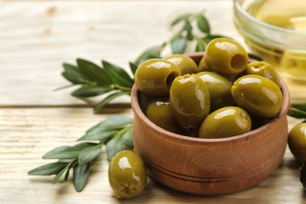 green olives with leaves in a wooden bowl with olive oil on a natural wooden table. close-up