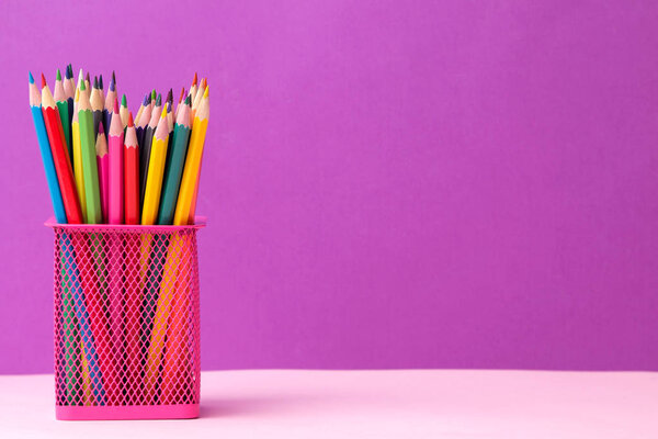 many colored pencils in a pink glass on a bright trendy lilac background. space for text