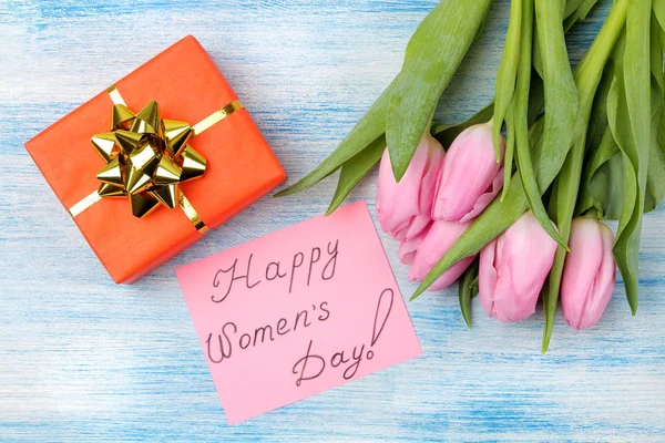 美丽的花束粉红色郁金香花 礼品盒和文字快乐的妇女节在纸上的蓝色木背景 从上面的意见 — 图库照片