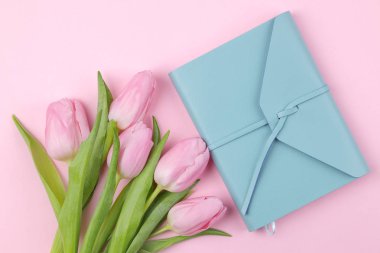 Bir buket güzel Pembe Lale çiçek ve trendy pembe bir arka plan üzerinde mavi bir defter. Bahar. tatil. Yukarıdan görüntülemek.
