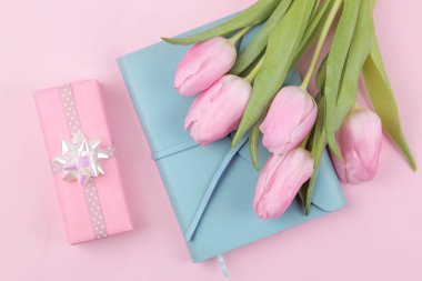 Bir buket güzel Pembe Lale çiçek ve trendy pembe bir arka plan üzerinde mavi bir defter. Bahar. tatil. Yukarıdan görüntülemek.