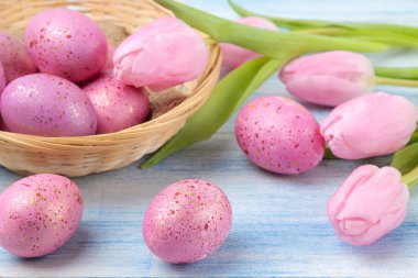 Paskalya. Pembe Paskalya bir sepete yumurta ve mavi ahşap bir masa üzerinde çiçekler. Mutlu paskalyalar. tatil.