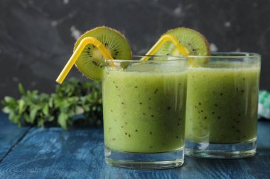 Kivi smoothies bir bardak taze kivi dilimleri üzerinde mavi bir ahşap masa yanında. meyve içki.