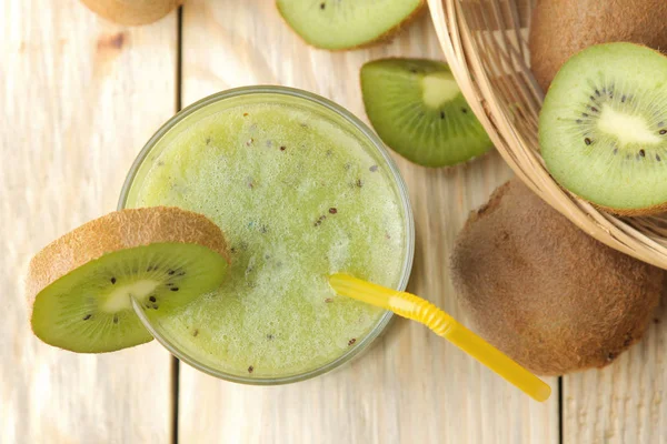 Kiwi smoothies in a glass next to fresh kiwi slices on a natural wooden table. top view