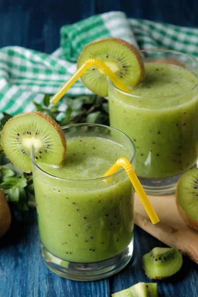 Kiwi smoothies in a glass next to fresh kiwi slices on a blue wooden table. fruit drink.