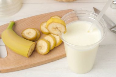 Bir milkshake yapma. bir muz milkshake, pişirme ve Mikser hafif bir arka plan üzerinde malzemeler ile plastik tek kullanımlık bardak