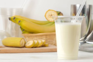 Bir milkshake yapma. bir muz milkshake, pişirme ve Mikser hafif bir arka plan üzerinde malzemeler ile plastik tek kullanımlık bardak