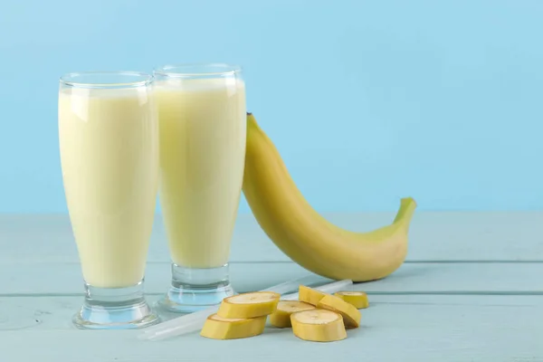 A glass with a banana milkshake and a fresh banana on a blue background. Making a milkshake.