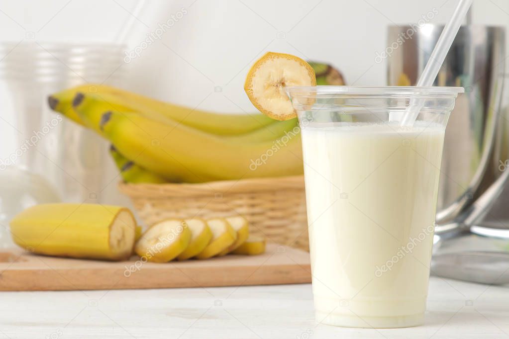 Making a milkshake. plastic disposable glass with a banana milkshake, ingredients for cooking and mixer on a light background