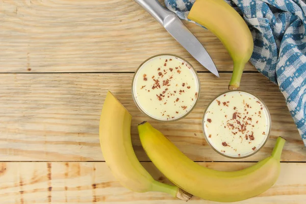 a glass with a banana milkshake, syrup and chocolate chips and a fresh banana on a natural wooden table. Making a milkshake. top view