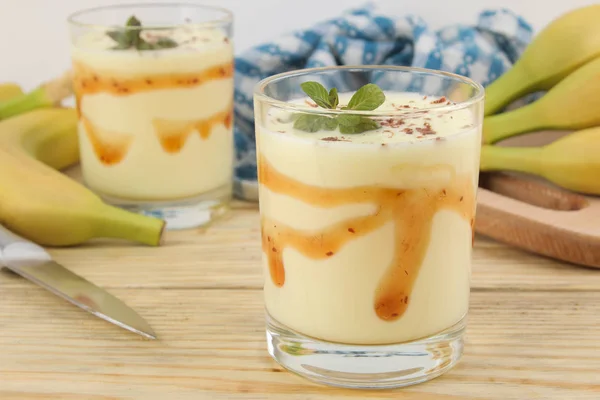 a glass with a banana milkshake, syrup and chocolate chips and a fresh banana on a natural wooden table. Making a milkshake.