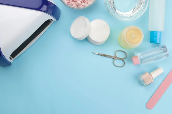 Manicure. nail polishes, UV lamp and various accessories and tools for manicure on a trendy blue background. top view