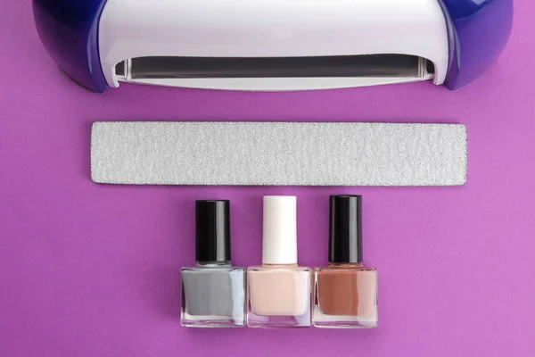Manicure. UV lamp and nail files and nail polishes on a trendy purple background. Manicure accessories and tools for nails. top view