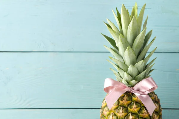 Ripe fruit pineapple with a pink bow on a blue wooden background. place for text. close-up