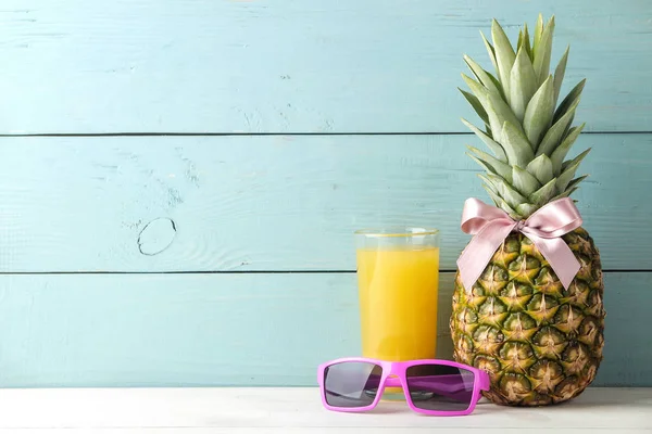 Ripe pineapple fruit with a pink bow, sunglasses and pineapple juice on a blue wooden background. place for text.