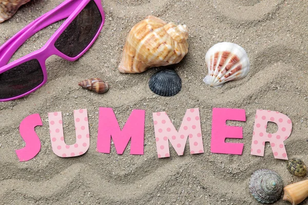 Inscription summer from paper of multi-colored letters and seashells and summer accessories on the sea sand. Summer. relaxation. vacation. top view