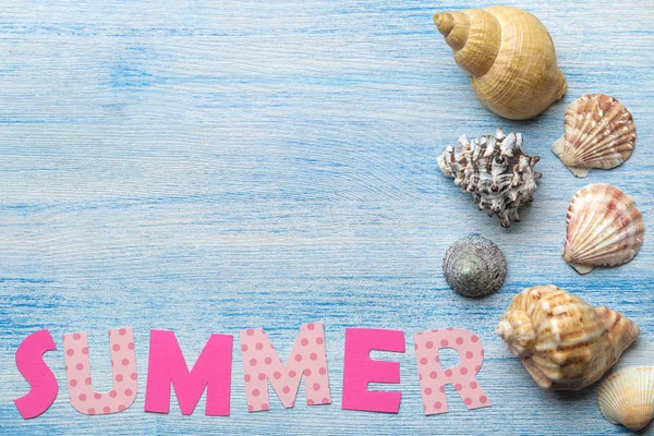 Inscription summer from paper of multi-colored letters and seashells and summer and sea accessories on a blue wooden table. Summer. relaxation. vacation. top view