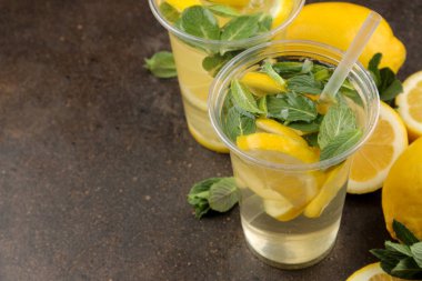 Kahverengi bir arka plan üzerinde plastik bardak nane ve limon ile ev yapımı limonata. Ferahlatıcı limonata içeceği.