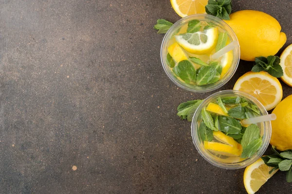 Homemade lemonade with mint and lemon in plastic glasses on a brown background. Refreshing lemonade drink. top view