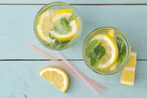 Homemade lemonade with mint and lemon in plastic glasses on a blue wooden background. Refreshing lemonade drink. top view