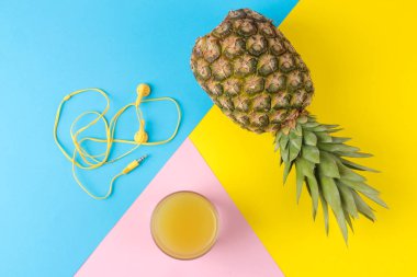 Parlak sarı, mavi ve pembe arka planda büyük olgun meyve ananas ve meyve suyu. Yaz. yukarıdan görünüm.