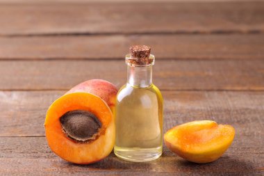 Kayısı çekirdeği yağı kahverengi ahşap arka plan üzerinde taze kayısı yanında.