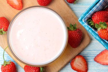 bir kavanozda lezzetli çilek yoğurt ve açık mavi ahşap masada taze olgun çilek. üst görünüm