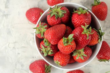 Olgun, lezzetli çilekler. Hafif beton bir masa üzerinde seramik bir kase kırmızı çilek. üst görünüm