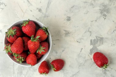 Olgun, lezzetli çilekler. Hafif beton bir masa üzerinde seramik bir kase kırmızı çilek. üst görünüm