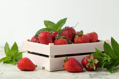 Olgun, lezzetli çilekler. Ahşap bir kutuda kırmızı çilek ve hafif beton masa üzerinde nane yaprağı.